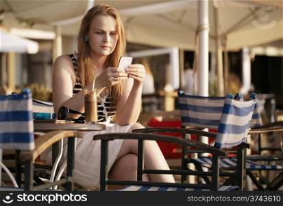 Attractive woman relaxing in a deckchair in the sun sending an sms or reading news on her mobile phone