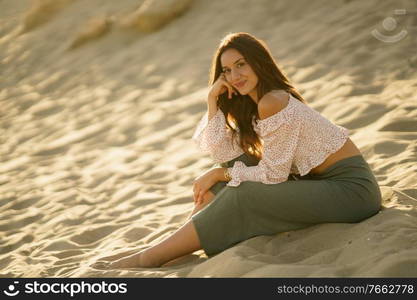 Attractive woman sitting on the sand of the beach looking at the horizon.. Attractive woman sitting on the sand of the beach