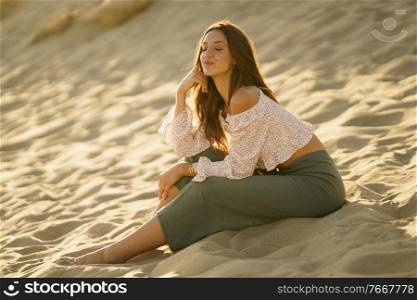 Attractive woman sitting on the sand of the beach with eyes closed. Young woman sitting on the sand of the beach with eyes closed