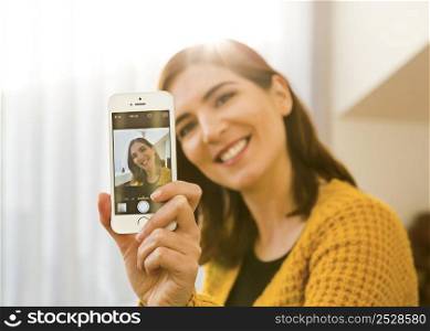 Attractive woman taking a photo of herself with her smartphone at home