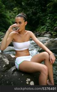 Attractive woman wearing a bikini and drinking water in the forest