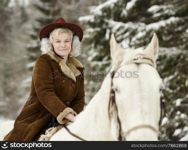 Attractive woman wearing a winter jacket and hat, she riding a white horse and she looks towards the camera