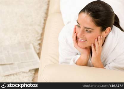 Attractive woman white bathrobe thinking lying on sofa in lounge