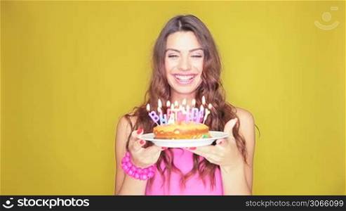 Attractive woman with long wavy brunette hair standing with her mouth open as she blows out her birthday candles on the cake