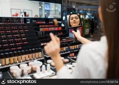 Attractive woman with mirror applies lipstick in cosmetics store. Buyer at the showcase in luxury beauty shop salon, female customer in fashion market. Woman with mirror applies lipstick in store