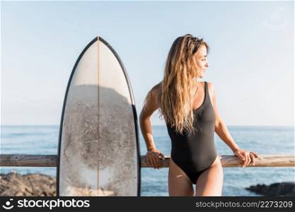 attractive woman with surfboard leaning fence