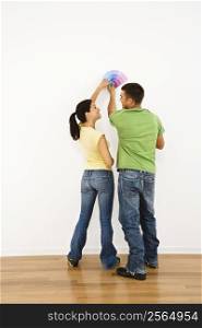 Attractive young adult couple holding color paint samples up to white wall.