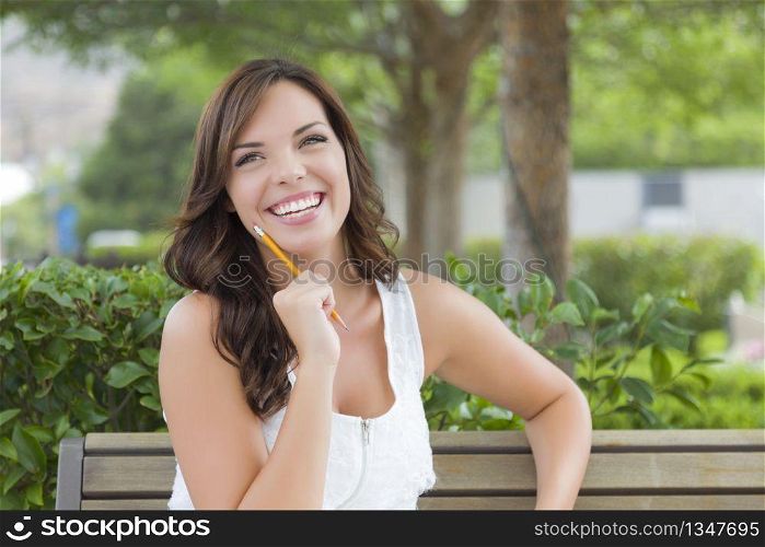 Attractive Young Adult Female Student on Bench Outdoors with Books and Pencil.