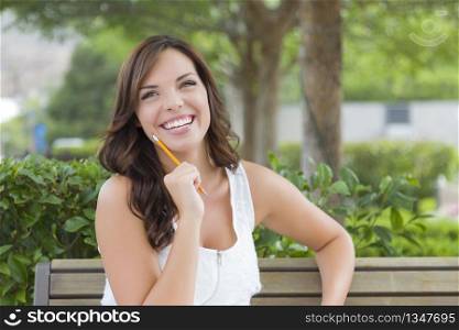 Attractive Young Adult Female Student on Bench Outdoors with Books and Pencil.