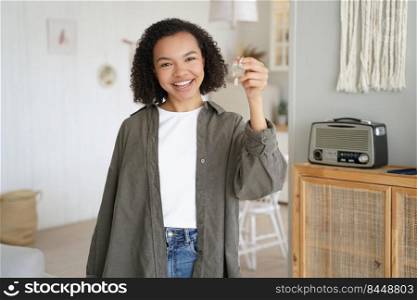 Attractive young african american girl is holding key from new home. Teenage tenant is happy. Teenager gets new apartment key. Mortgage loan and real estate purchase conceptual image.. African american teenager gets apartment key. Mortgage and real estate purchase conceptual image.