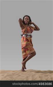 Attractive young African fashion model standing on sand on gray studio background