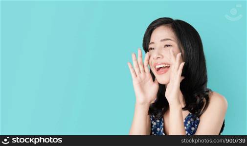 Attractive young asian woman announcing with hands to the mouth and telling a secret, isolated on light blue background