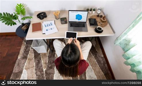 Attractive young beautiful asian woman working with laptop and document while sitting at the indoors living room office as a freelancer, e-coaching working, remotely or work from home concept