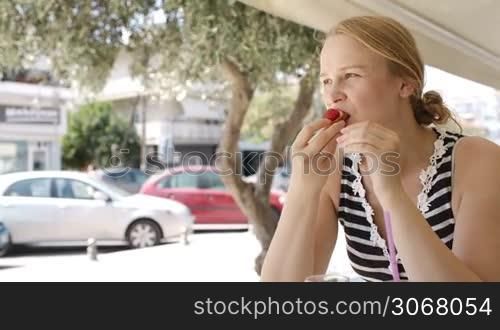 Attractive young blond woman eating refreshments in a cafeteria overlooking an urban street