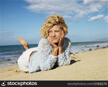 Attractive young blond woman lying in sand on Maui, Hawaii beach with head resting on hands.