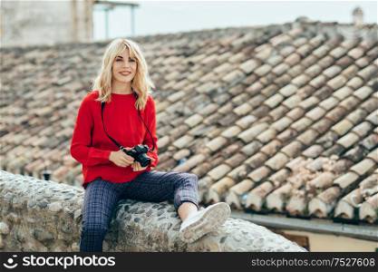 Attractive young blond woman taking photographs with an old slr camera in a beautiful city. Blonde happy woman sitting on urban steps.. Young woman taking photographs with an old camera in a beautiful city.