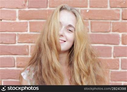 Attractive young blonde on the background of a brick wall smiling closeup