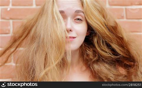Attractive young blonde with long hairs on the background of a brick wall.