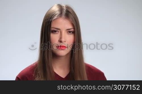 Attractive young brunette woman with sad expression looking at the camera on white background. Beautiful girl with deep brown eyes staring at you with upset and disappointed look.