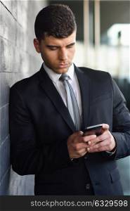 Attractive young businessman on the phone in an office building wearing black suit and tie. Man with blue eyes