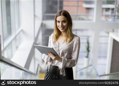 Attractive young businesswoman using a digital tablet while standing on the stairs in the office