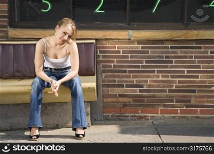 Attractive young Caucasian woman sitting on bench outside.
