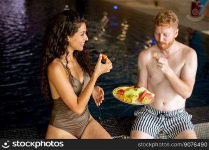 Attractive young couple enjoying in indoor swimming pool on vacation and eating fresh fruits