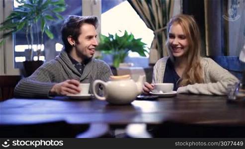 Attractive young couple having great time together while relaxing in cafe and talking. Cheerful teenagers spending leisure at restaurant, chatting drinking tea and smiling.