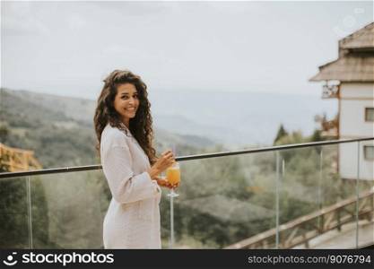 Attractive young curly hair woman relaxing and drinking fresh orange juice on the outdoor terrace