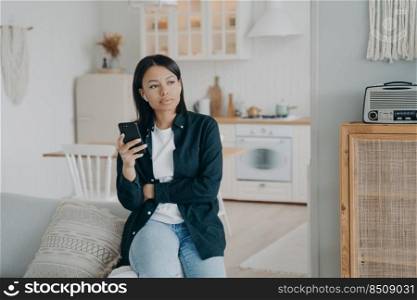 Attractive young european woman enjoying music listening in airpods. Pensive girl in earphones relaxing and dreaming. Lady sitting on couch and having nice weekend morning. Emotions and entertainment.. Pensive young woman enjoying music listening in airpods. Girl in earphones relaxing and dreaming.
