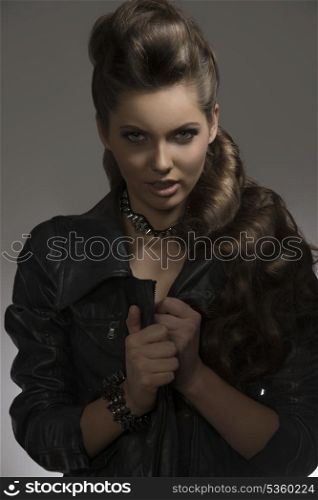 attractive young female posing with fashion dark look, black leather jacket and rock accessories with aggressive expression