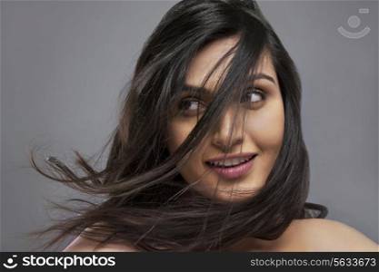 Attractive young female with hair blowing over face against colored background