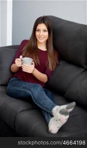 Attractive young girl lying on the sofa drinking tea