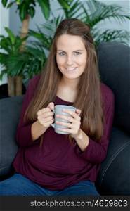 Attractive young girl sitting on the sofa drinking tea&#xA;
