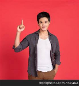 Attractive young handsome asian man in casual t-shirt pointing up with his finger isolated on red background in studio.