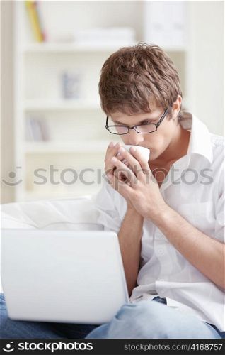 Attractive young man drinking and looking at laptop