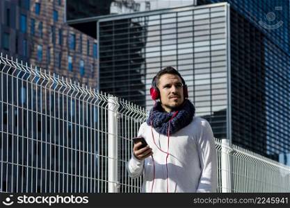 Attractive young man listening music by headphones while holding a mobile phone outdoor