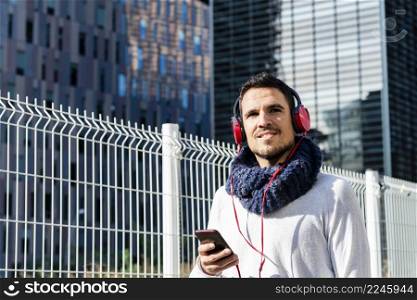 Attractive young man listening music by headphones while holding a mobile phone outdoor
