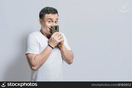 Attractive young man smiling with his cell phone, Attractive person smiling at the camera while holding his cell phone on isolated background, Young man covering his mouth with cell phone