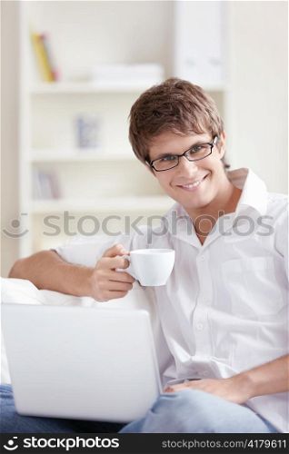 Attractive young man with a cup and laptop