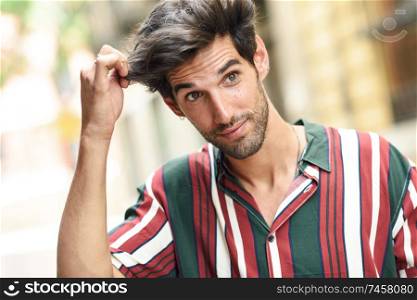Attractive young man with dark hair and modern hairstyle wearing casual clothes in urban background.. Attractive young man with dark hair and modern hairstyle wearing casual clothes outdoors