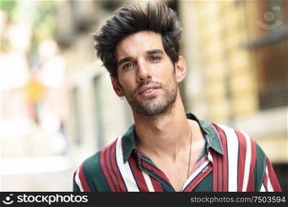 Attractive young man with dark hair and modern hairstyle wearing casual clothes in urban background.. Attractive young man with dark hair and modern hairstyle wearing casual clothes outdoors