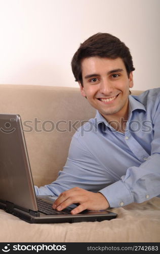 attractive young man with laptop computer lying on the couch at home