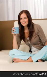 Attractive young woman at modern home sitting sofa drink coffee