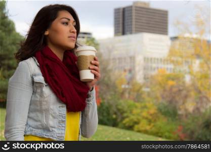 Attractive young woman enjoying coffee during fall with the city in the background