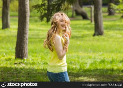 Attractive young woman enjoying her time walking in summer park at sunny day. Young woman walking in park