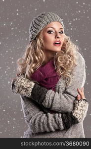 attractive young woman in a winter fashion shot wearing a wool cap, a grey woolen sweater and a purple scarf