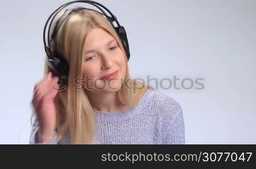 Attractive young woman in headphones enjoying music on white background. Happy teenage girl looking at camera silently saying what and laughing. Girl lifting one earcups with smile and noding then putting earcup back on ear and continues listening.