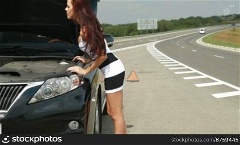 Attractive young woman looking under the car hood