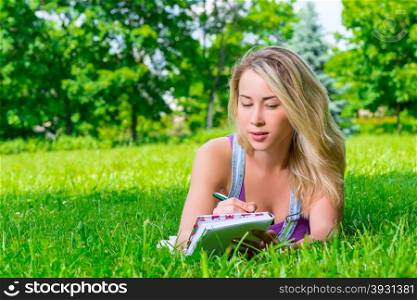 attractive young woman making notes in a notebook lying on the grass